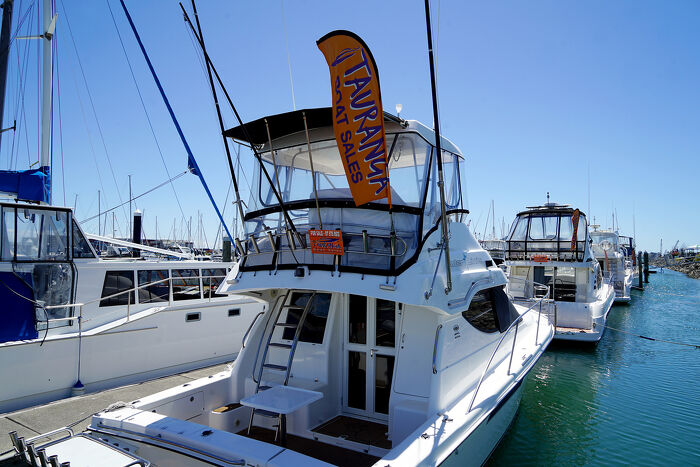 Powerboat moored at Tauranga Bridge Marina with a Tauranga Boat Sales flag and signage, Bay of Plenty, New Zealand.
