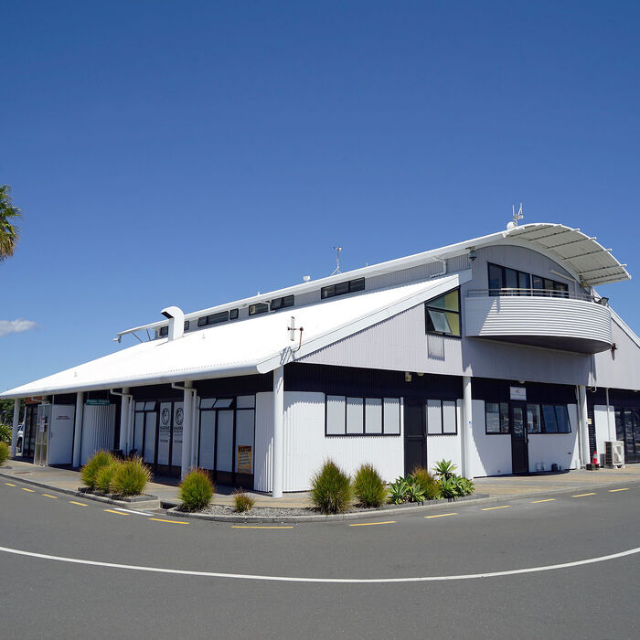 Modern curved-roof building at Tauranga Bridge Marina, Bay of Plenty, New Zealand, housing offices and marine services under a clear blue sky.