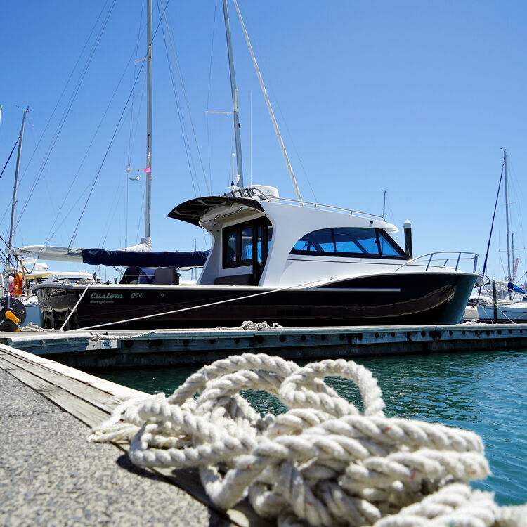 Stylish black and white launch boat named 'Custom 950' moored at Tauranga Bridge Marina, with coiled rope in the foreground.